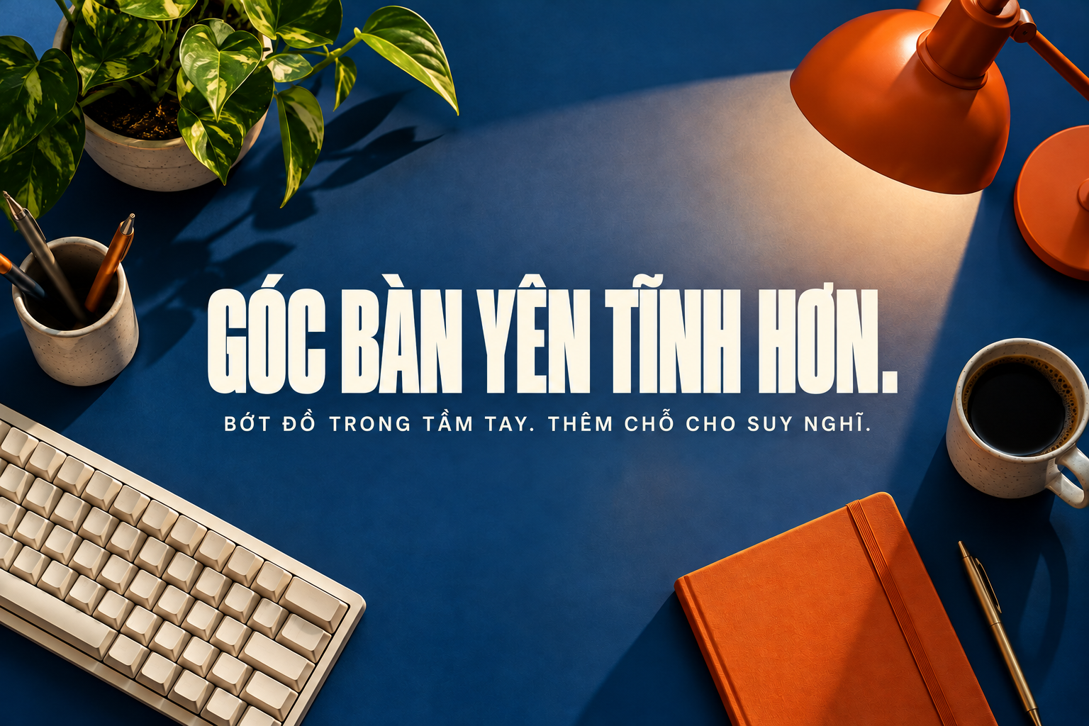 Góc bàn yên tĩnh: mặt bàn xanh cô-ban, bàn phím màu kem và sổ cam.